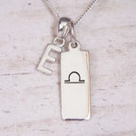 Silver Initial and Libra Zodiac Necklace with a letter E pendant and engraved Libra bar, flat lay on light wood