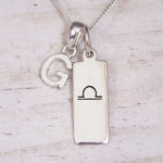 Silver Initial and Libra Zodiac Necklace with a letter G pendant and engraved Libra bar, flat lay on light wood