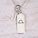 Silver Initial and Libra Zodiac Necklace with a letter J pendant and engraved Libra bar, flat lay on light wood