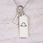 Silver Initial and Libra Zodiac Necklace with a letter L pendant and engraved Libra bar, flat lay on light wood