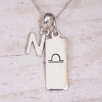 Silver Initial and Libra Zodiac Necklace with a letter N pendant and engraved Libra bar, flat lay on light wood