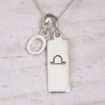 Silver Initial and Libra Zodiac Necklace with a letter O pendant and engraved Libra bar, flat lay on light wood