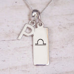 Silver Initial and Libra Zodiac Necklace with a letter P pendant and engraved Libra bar, flat lay on light wood