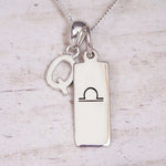 Silver Initial and Libra Zodiac Necklace with a letter Q pendant and engraved Libra bar, flat lay on light wood