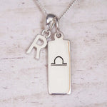 Silver Initial and Libra Zodiac Necklace with a letter R pendant and engraved Libra bar, flat lay on light wood