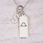 Silver Initial and Libra Zodiac Necklace with a letter S pendant and engraved Libra bar, flat lay on light wood