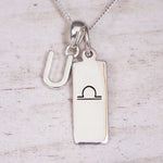Silver Initial and Libra Zodiac Necklace with a letter U pendant and engraved Libra bar, flat lay on light wood