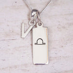 Silver Initial and Libra Zodiac Necklace with a letter V pendant and engraved Libra bar, flat lay on light wood