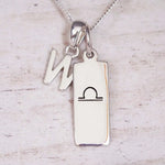 Silver Initial and Libra Zodiac Necklace with a letter W pendant and engraved Libra bar, flat lay on light wood