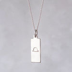 Silver necklace with a rectangular libra zodiac glyph pendant on a grey background