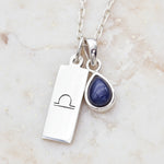 Silver necklace with tear drop natural sapphire gemstone pendant and libra zodiac pendant on a textured background