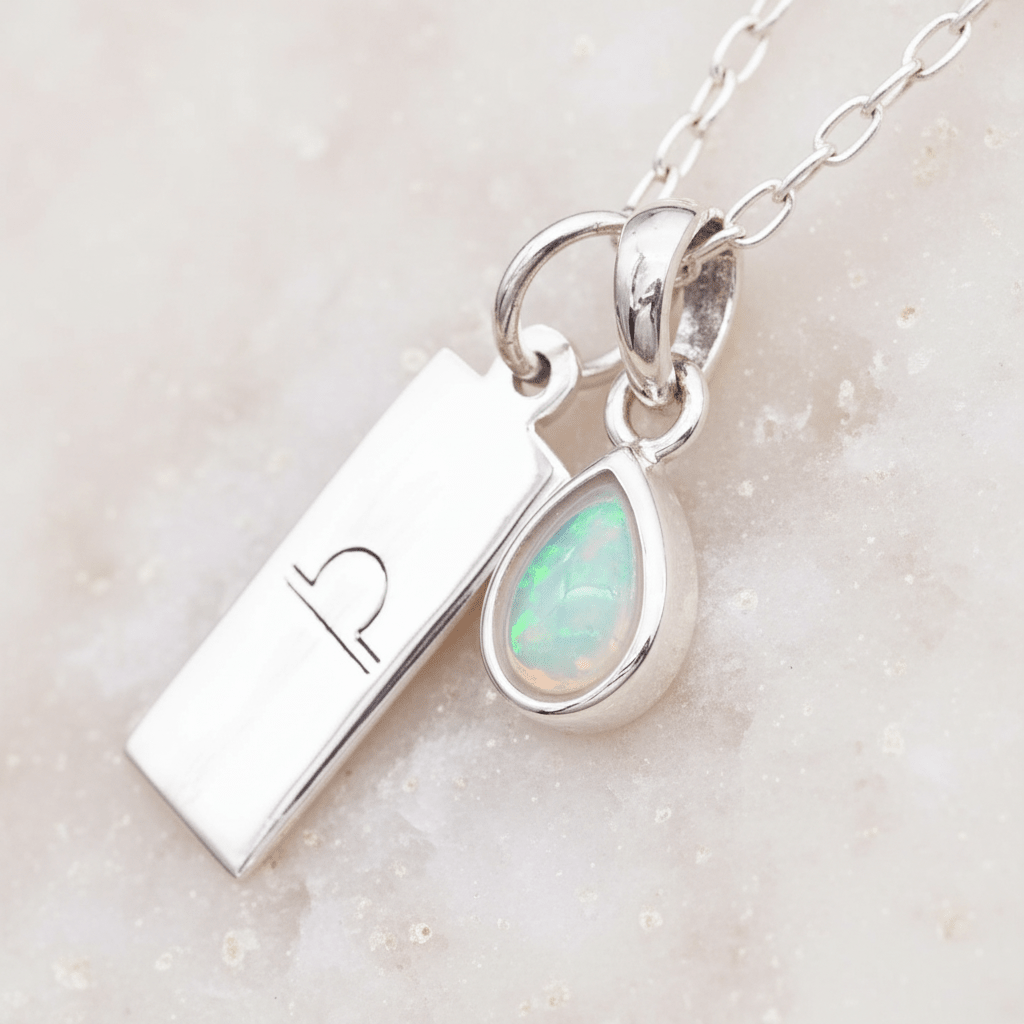 Silver necklace with a libra zodiac pendant and teardrop-shaped opal pendant on a light background