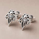 A pair of silver geometric flower stud earrings with openwork detailing, displayed on a neutral beige background.
