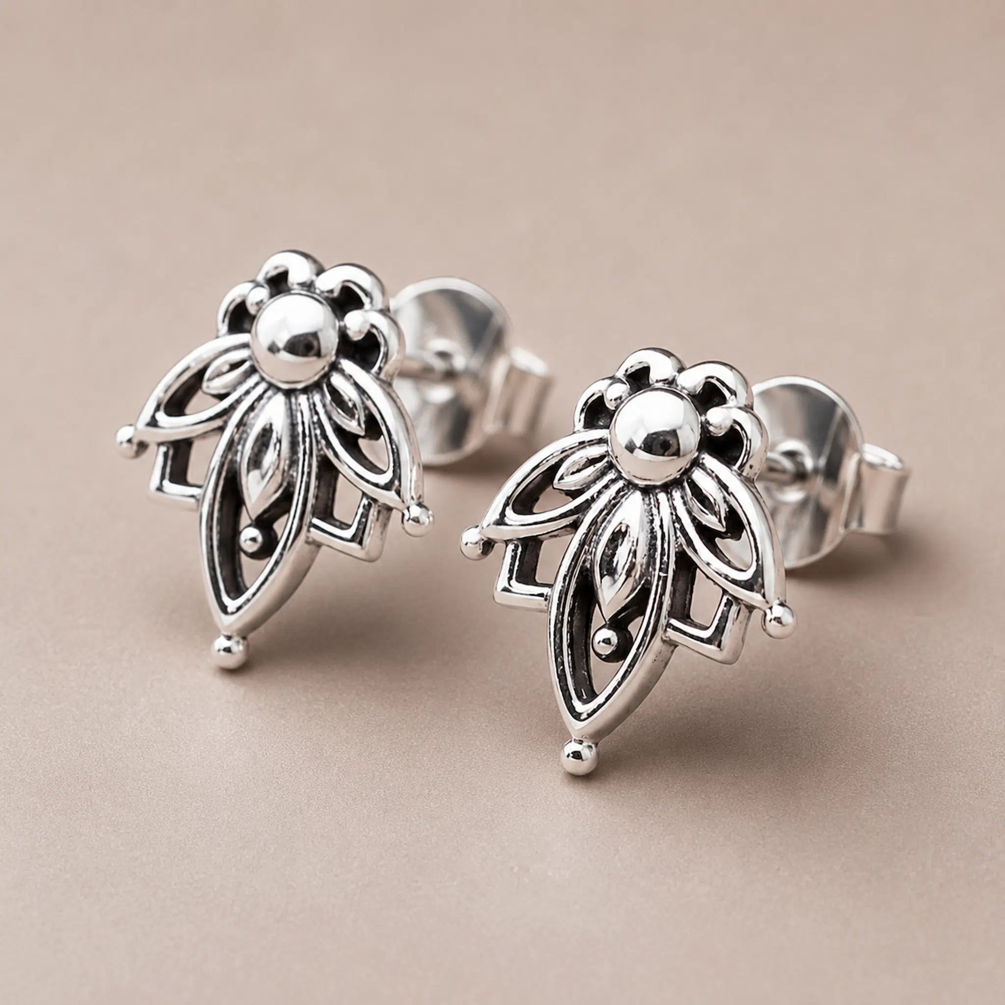 A pair of silver geometric flower stud earrings with openwork detailing, displayed on a neutral beige background.