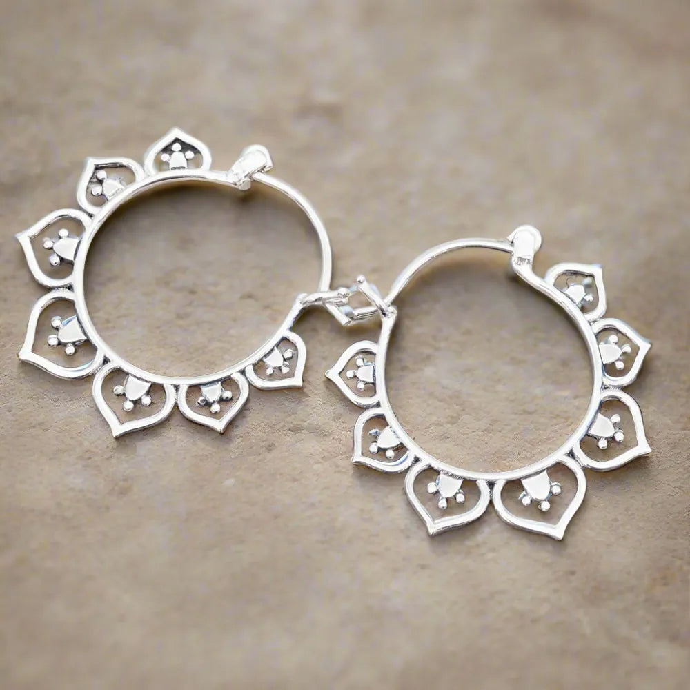 Silver hoop earrings with intricate designs on a beige background