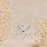 A silver pendant moonstone necklace featuring a central round iridescent moonstone surrounded by three teardrop-shaped metal settings, suspended from a delicate chain. The necklace is displayed against a soft beige background decorated with dried baby's breath flowers.