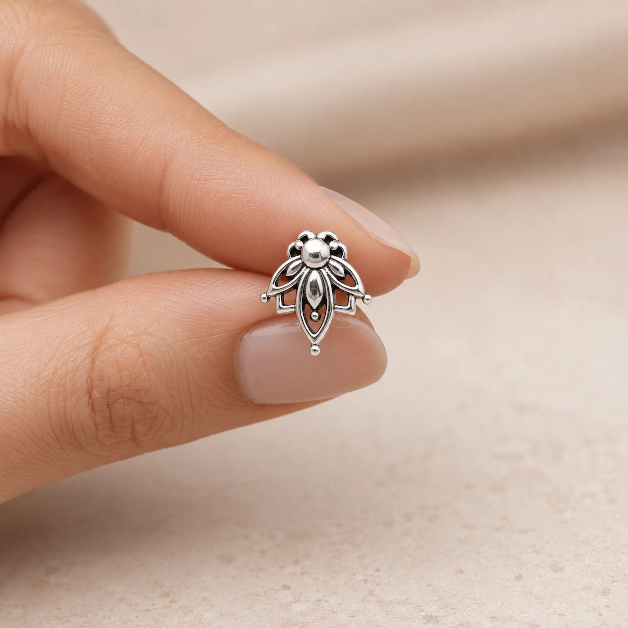 A silver lotus-shaped ring being held between fingers to show its scale, set against a soft, warm beige background.