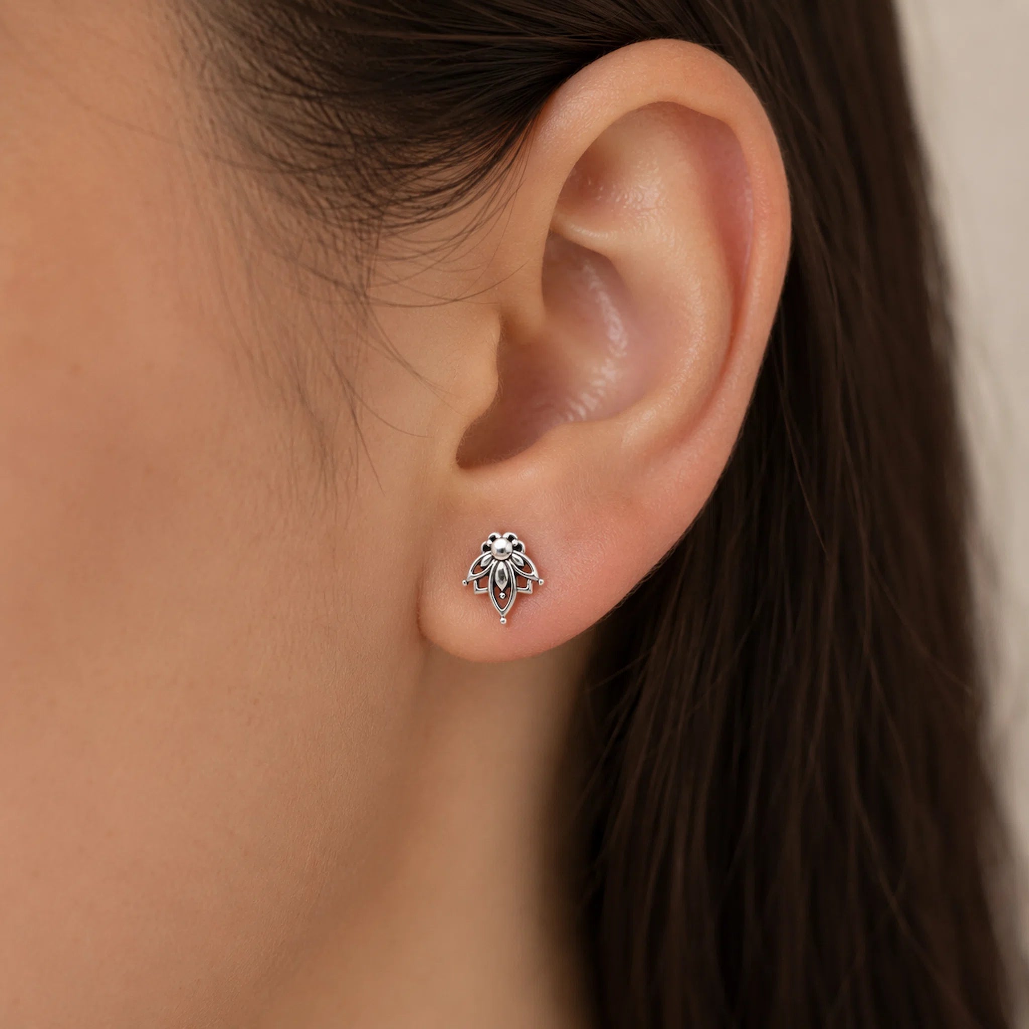 A close-up of a person's ear wearing a small silver lotus stud earring.