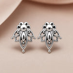 A pair of silver stud earrings with an intricate, symmetrical openwork lotus design, displayed on a soft beige surface.