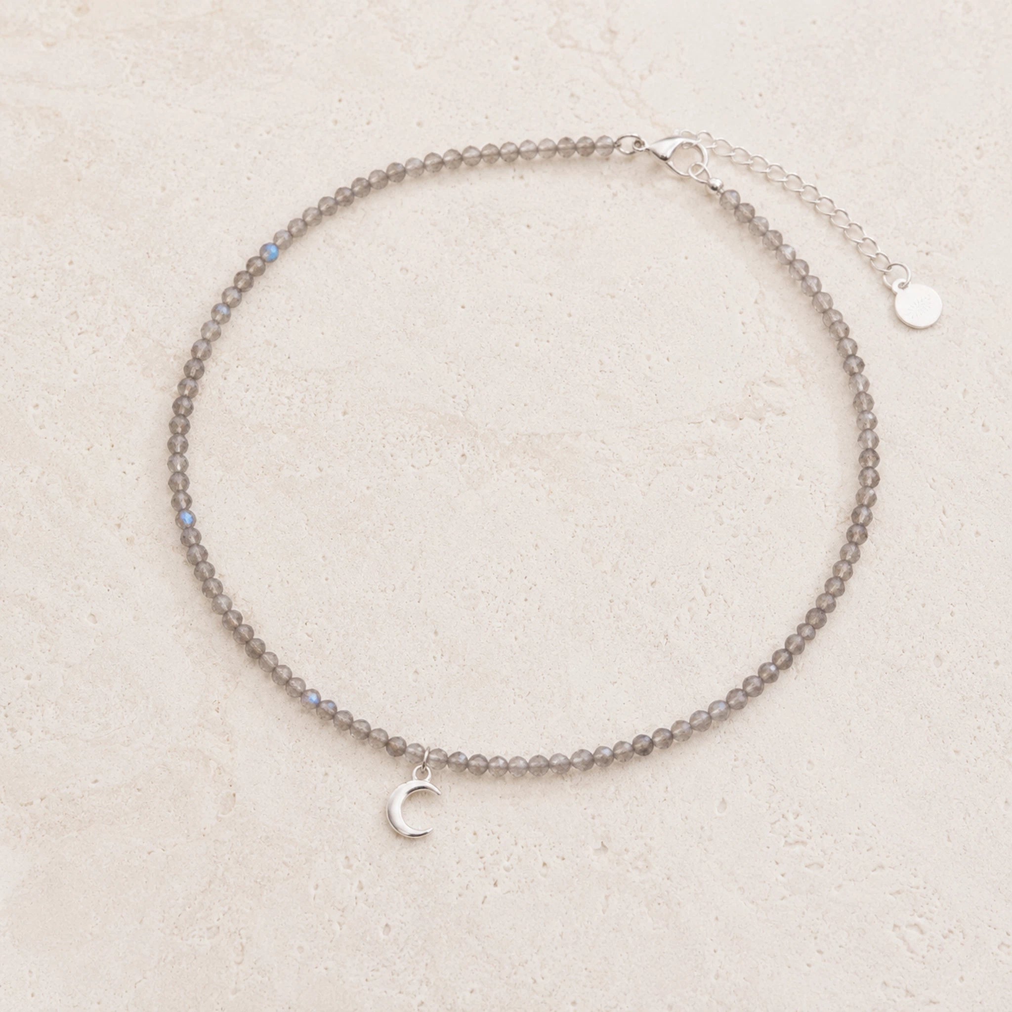 dainty natural labradorite beaded necklace with a silver crescent moon charm on a white background.