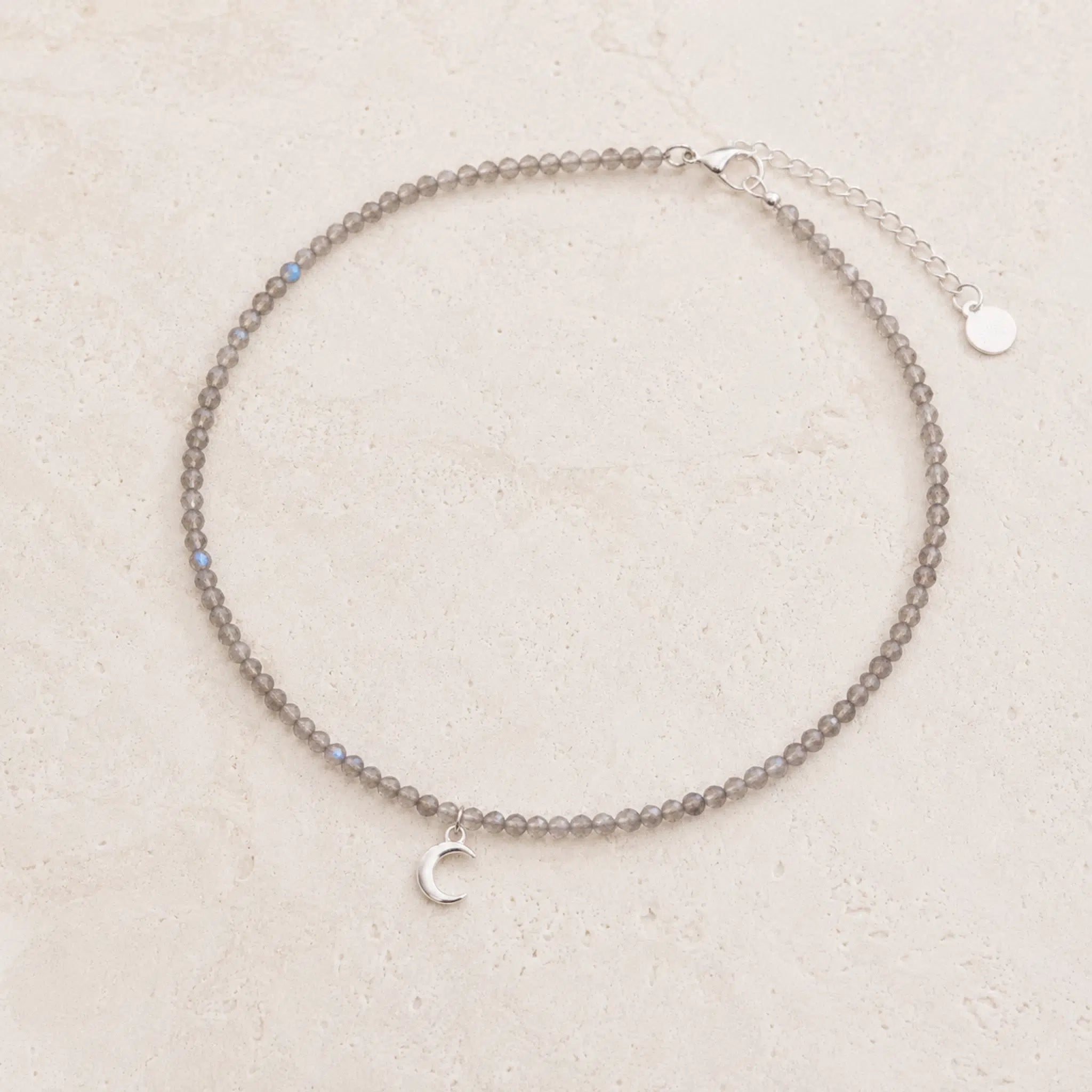 dainty natural labradorite beaded necklace with a silver crescent moon charm on a white background.