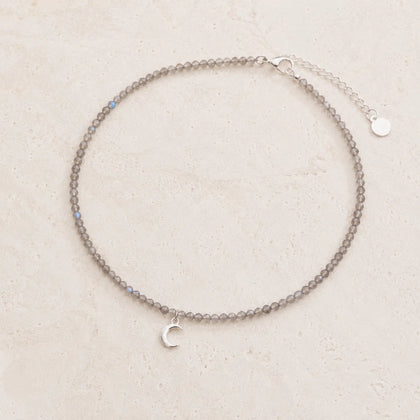 dainty natural labradorite beaded necklace with a silver crescent moon charm on a white background.