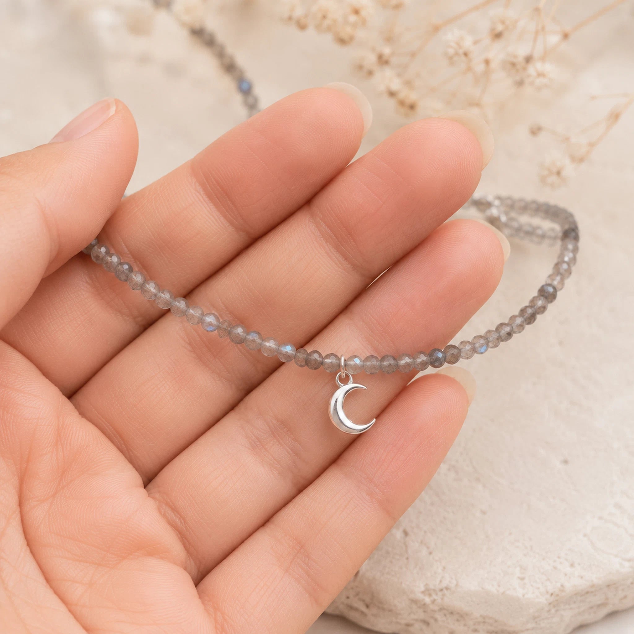 hand holding a dainty ntural labradorite beaded necklace with a silver crescent moon charm.
