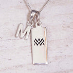 Sterling Silver M Initial and Aquarius Necklace on a fine silver chain against a light wooden background