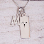 Sterling Silver M Initial pendant and Aries necklace on a fine silver chain on a light wooden background