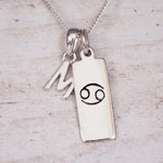 Sterling Silver M Initial Cancer Zodiac Star Sign Necklace on a fine silver chain against a light wooden background