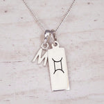 Sterling silver W initial and GeminI Necklace on a fine silver chain on a light wooden background