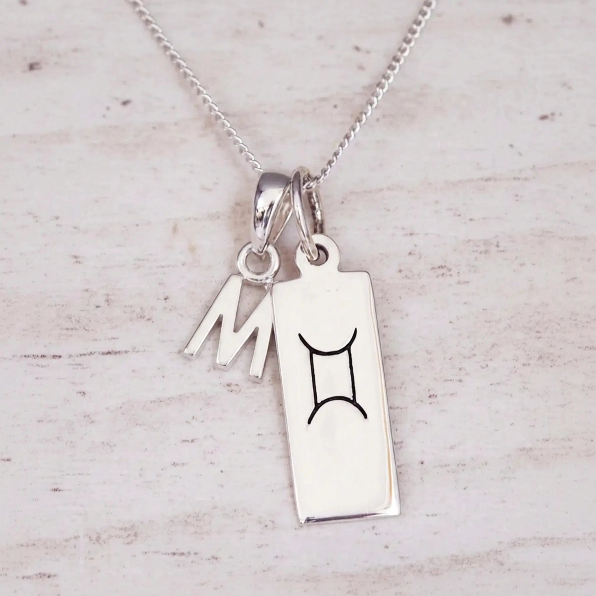 Sterling silver W initial and GeminI Necklace on a fine silver chain on a light wooden background