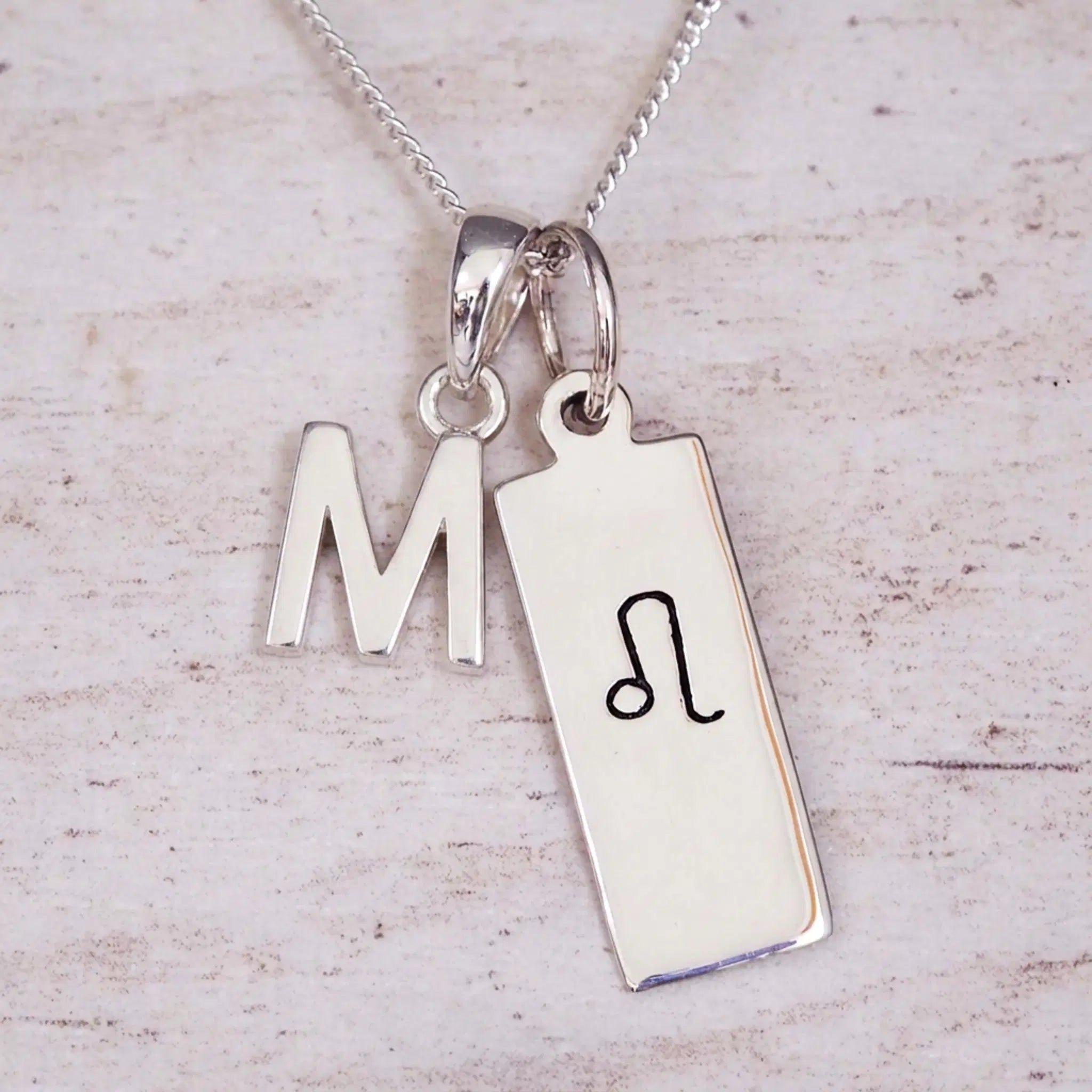 sterling silver initial m leo zodiac star sign pendant necklace against a light wooden background