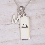 sterling silver initial m libra zodiac star sign pendant necklace against a light wooden background