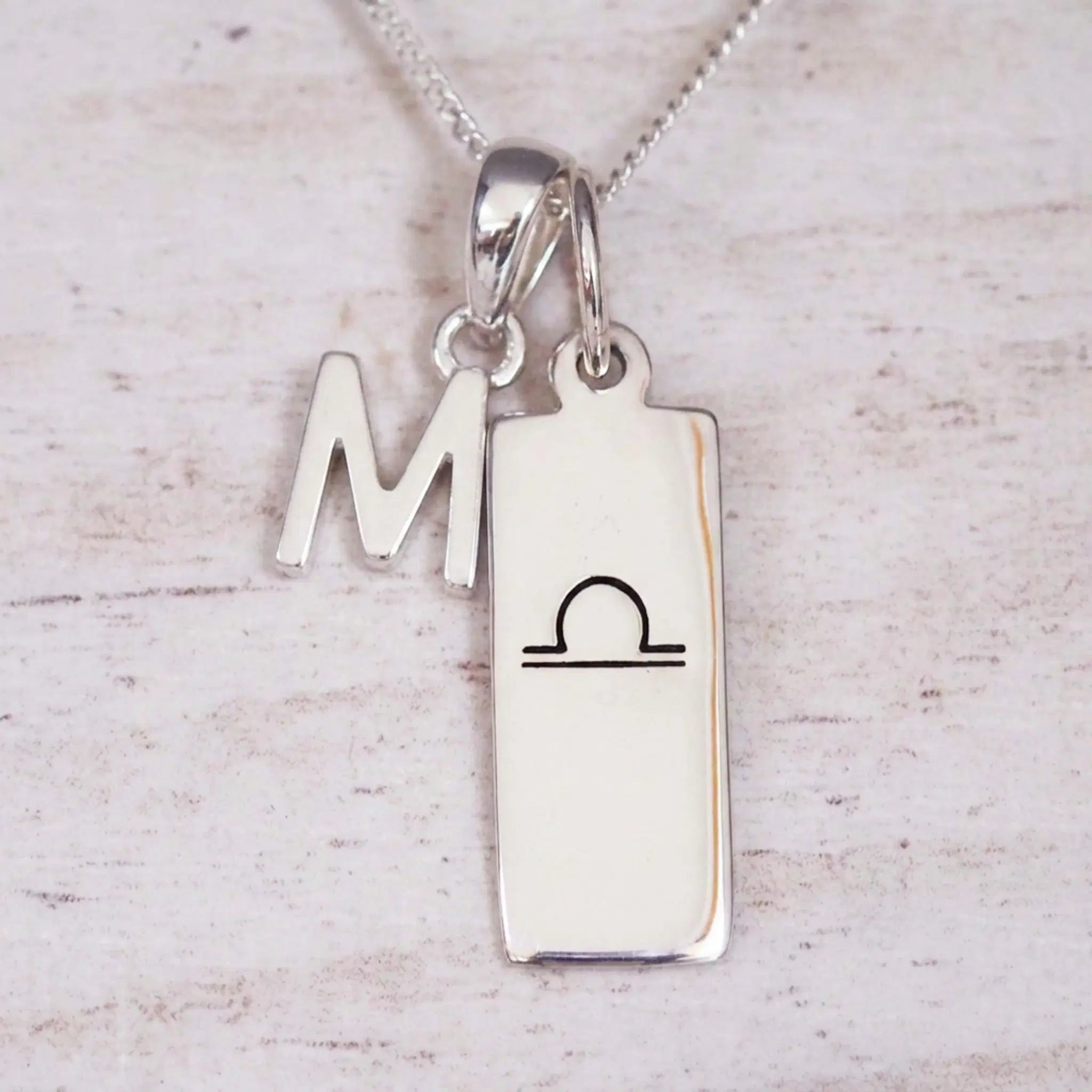sterling silver initial m libra zodiac star sign pendant necklace against a light wooden background
