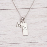 sterling silver M initial Pisces Necklace on a fine silver chain against a light wooden background