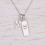 Sterling silver M initial Pendant and Taurus Necklace on a fine silver chain on a light wooden background