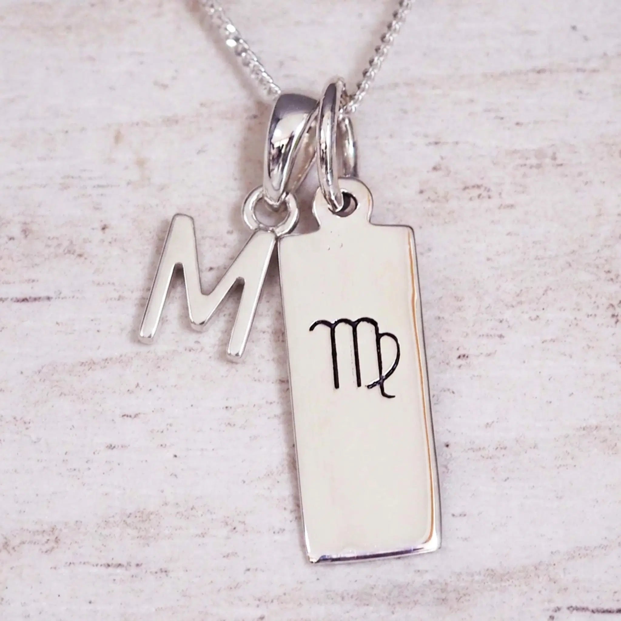 sterling silver initial m virgo zodiac star sign pendant necklace against a light wooden background