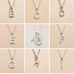 Collection of silver necklaces with letter pendants B to I on a beige background, as personalised initial options for a March Birthstone Aquamarine Necklace.