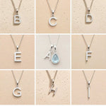 Collection of silver necklaces with letter pendants B to I on a beige background, as personalised initial options for a March Birthstone Aquamarine Necklace.