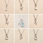 Collection of silver necklaces with letter pendants J to Q on a beige background, as personalised initial options for a March Birthstone Aquamarine Necklace.