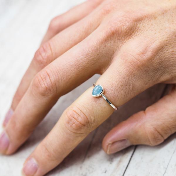 Hand wearing a sterling silver ring with a tear drop shaped natural aquamarine gemstone on a light wooden surface