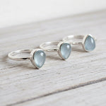 Three silver rings with heart-shaped light blue natural aquamarine gemstones on a wooden surface