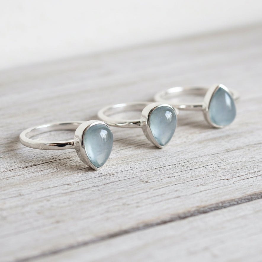 Three silver rings with heart-shaped light blue natural aquamarine gemstones on a wooden surface
