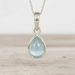march birthstone necklace Teardrop-shaped natural aquamarine gemstone pendant on a sterling silver chain against a wooden background