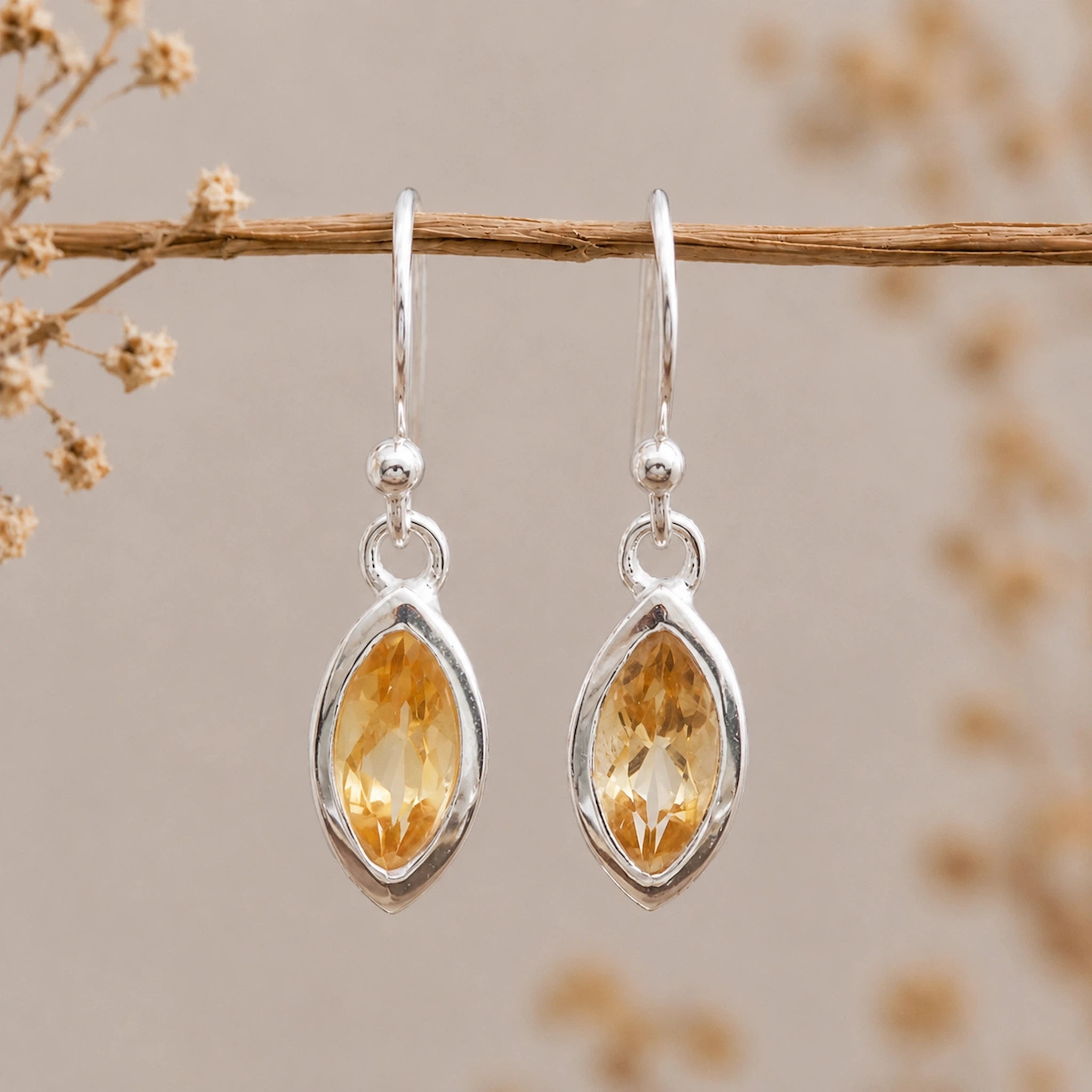 Silver french hook earrings with yellow marquise citrine gemstones hanging on a branch against a neutral background