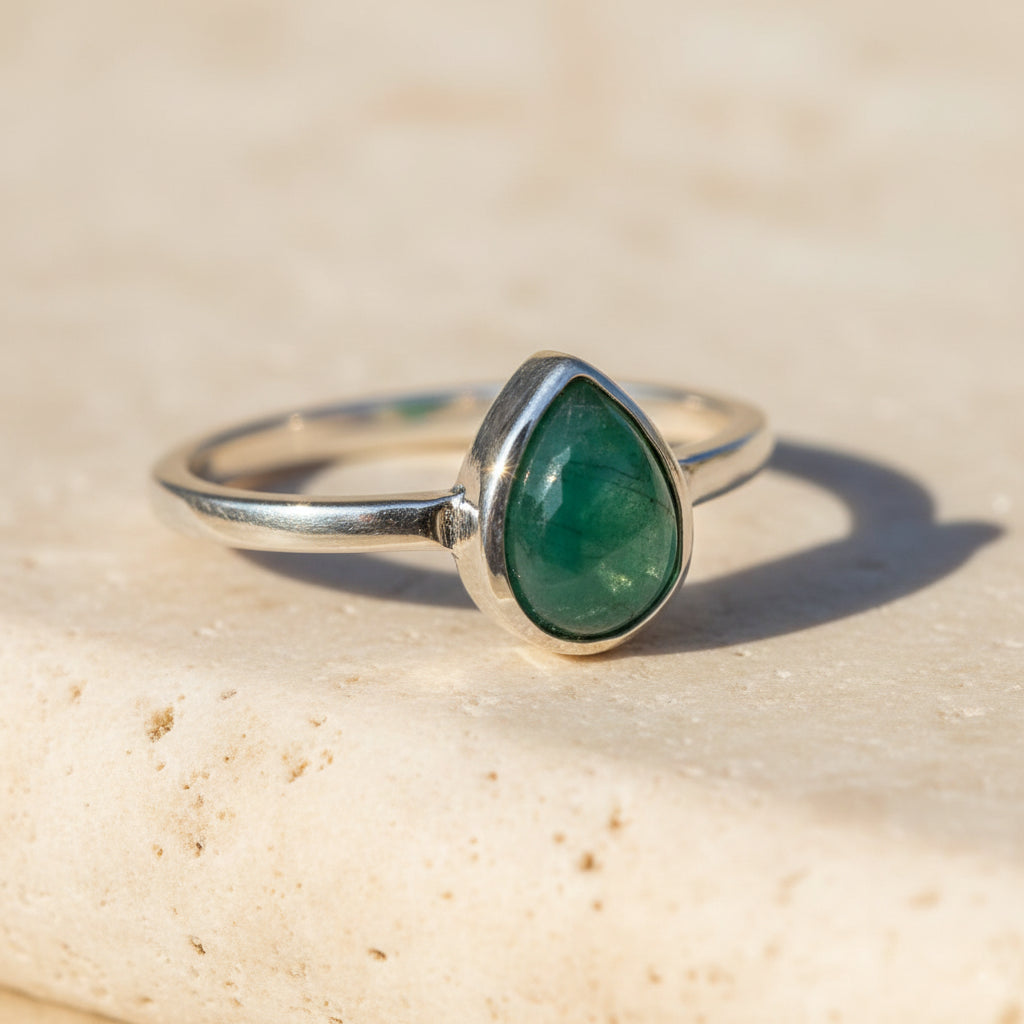 Silver ring with a green emerald teardrop-shaped gemstone on a wooden surface
