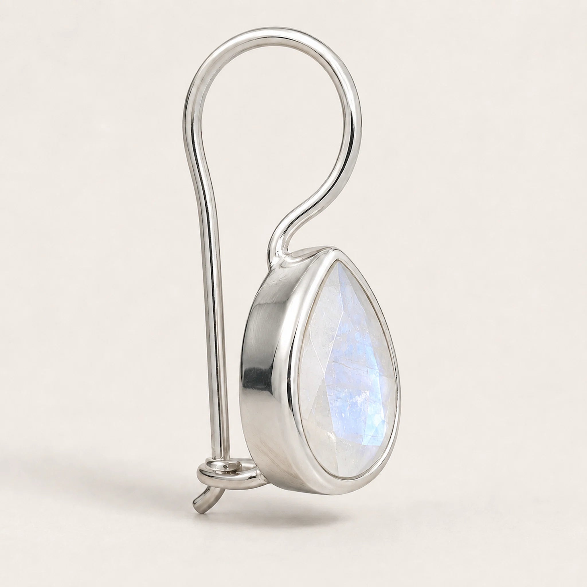 A silver-toned teardrop pendant with a faceted iridescent moonstone inlay, suspended from a curved silver wire loop, shown on a light beige background.