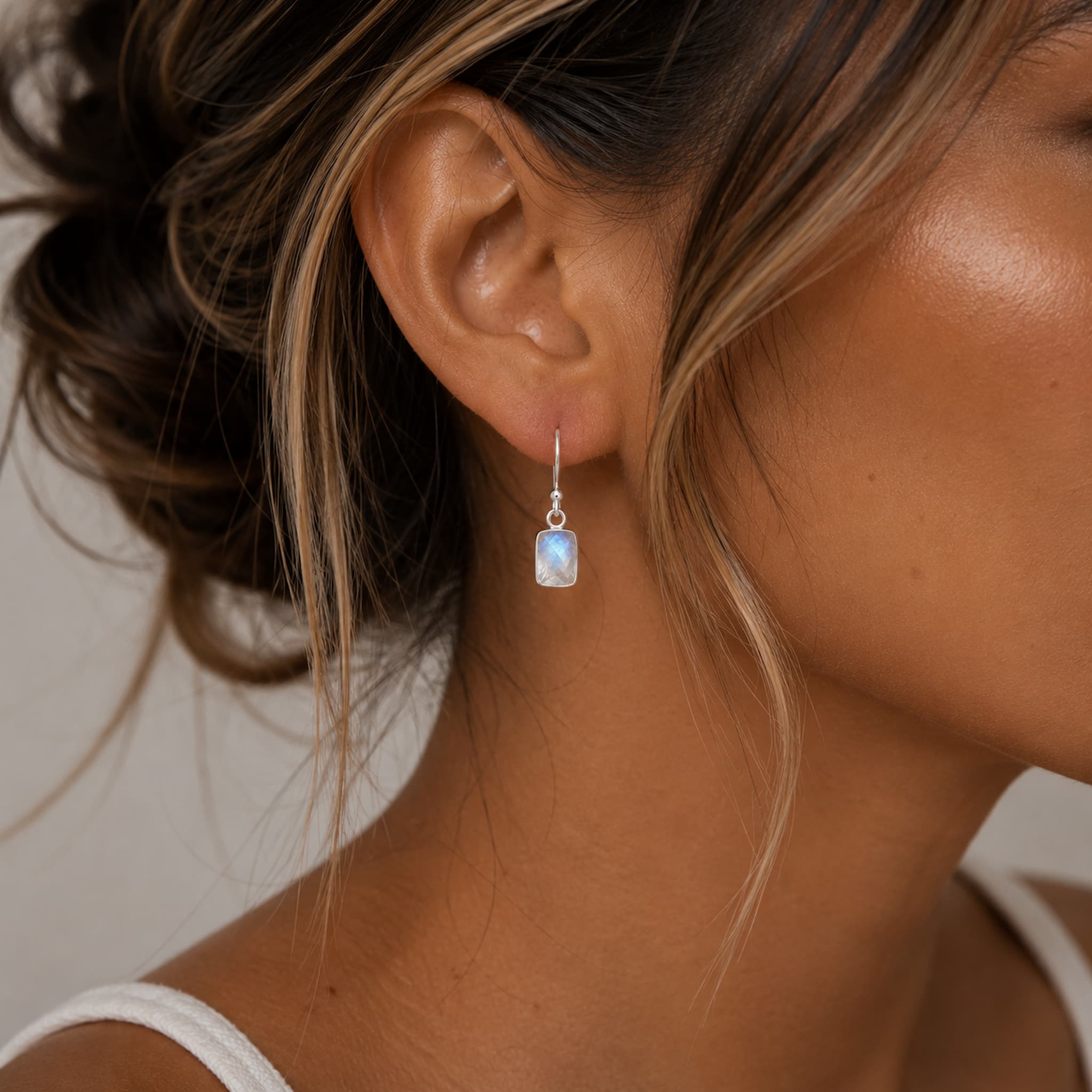 sterling silver moonstone earrings with rectangle natural faceted rectangle moonstones which are bezel set, hanging from classic french hooks being worn.