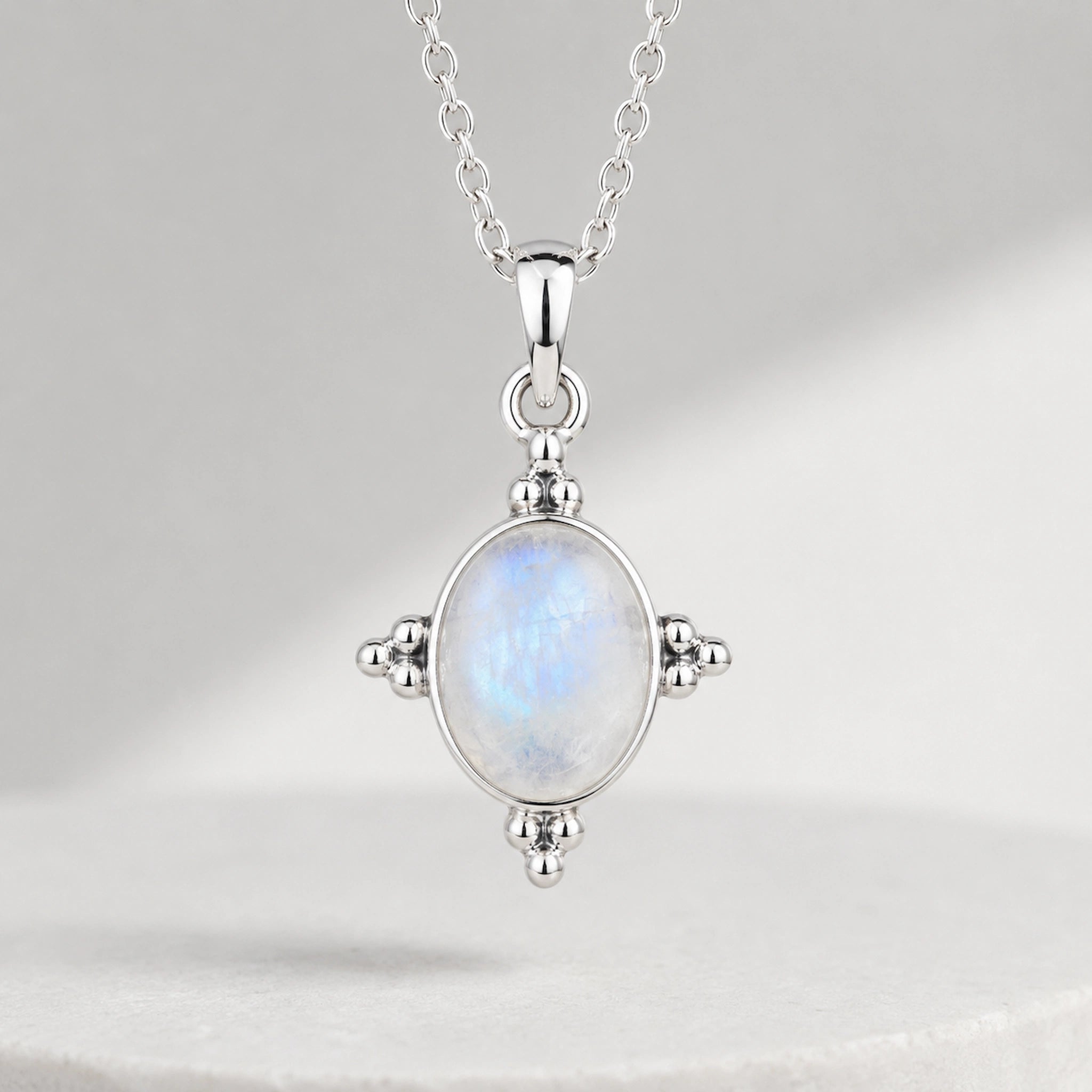 A sterling silver pendant necklace featuring an oval-shaped iridescent moonstone with blue and white play-of-color, set in a four-pronged silver bezel on a delicate chain.